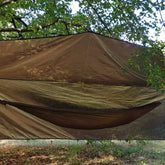 Bushmen Thermo Tarp 4×3 Olive hanging between trees, showcasing its durable, water-resistant design.